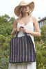 Model holding Marbella tote in Navy with natural stripes in front of wildflowers