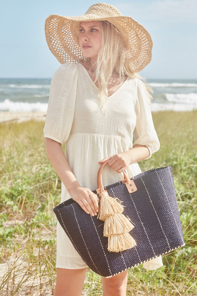 Model on the beach wearing our Sienna sun hat in Natural and our Marley sisal beach tote in Navy
