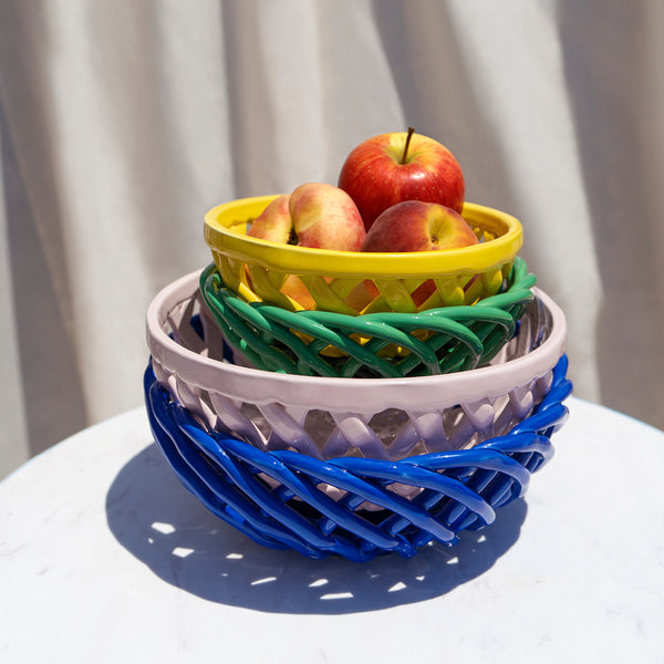 Stack of four glazed ceramic baskets in blue, pink, green, and yellow with some fruit