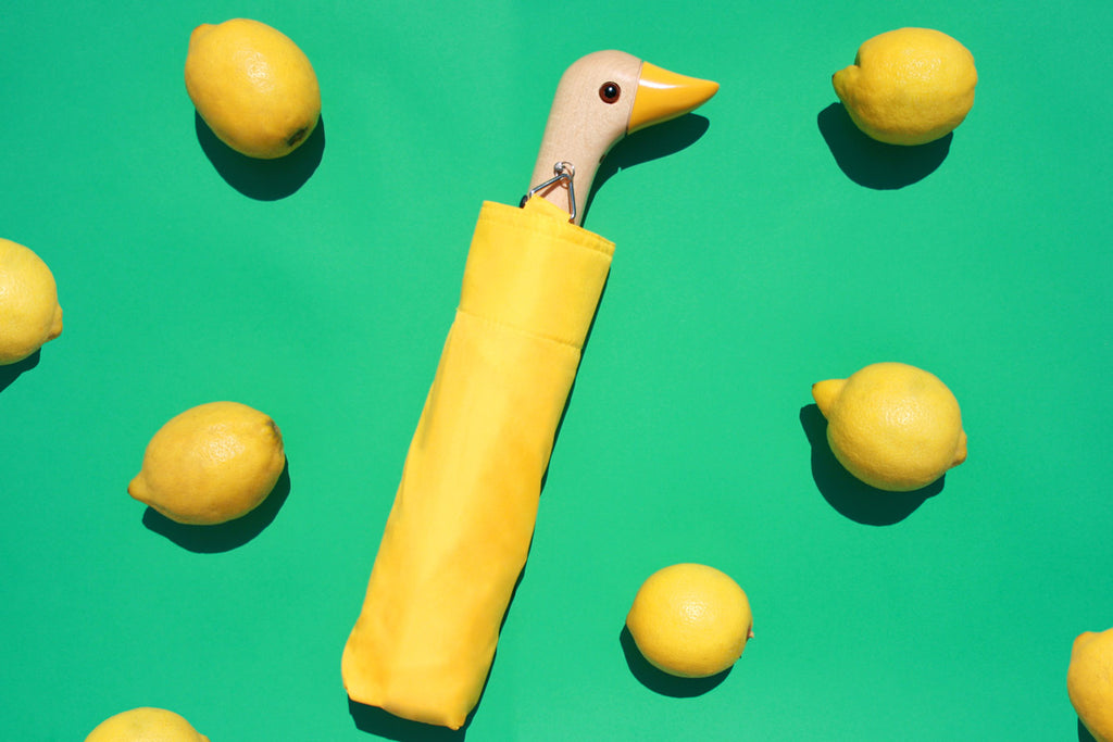 Yellow umbrella with a duck head handle posed with lemons