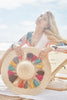 Model sitting on a beach chair holding our Paloma raffia sun hat in Natural with Multi Tassels