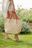Model holding natural colored crocheted carryall with snap closure, cotton lining & leather straps