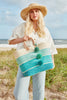 Model on the beach wearing our Stella raffia sun hat in Natural and our Samana sisal carryall tote in Aqua