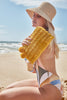 Model kneeling on the beach in a swimsuit wearing our Bella raffia sun hat in Natural and our Sasha raffia clutch in Sunflower