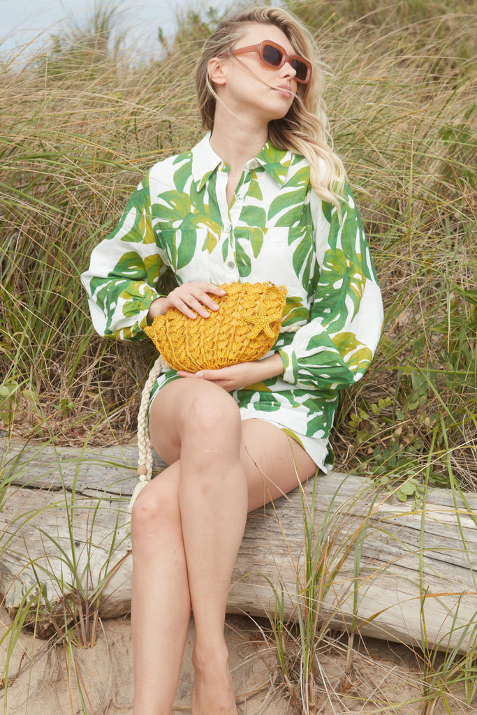 Model sitting on a driftwood log holding our Shelley clutch in Sunflower