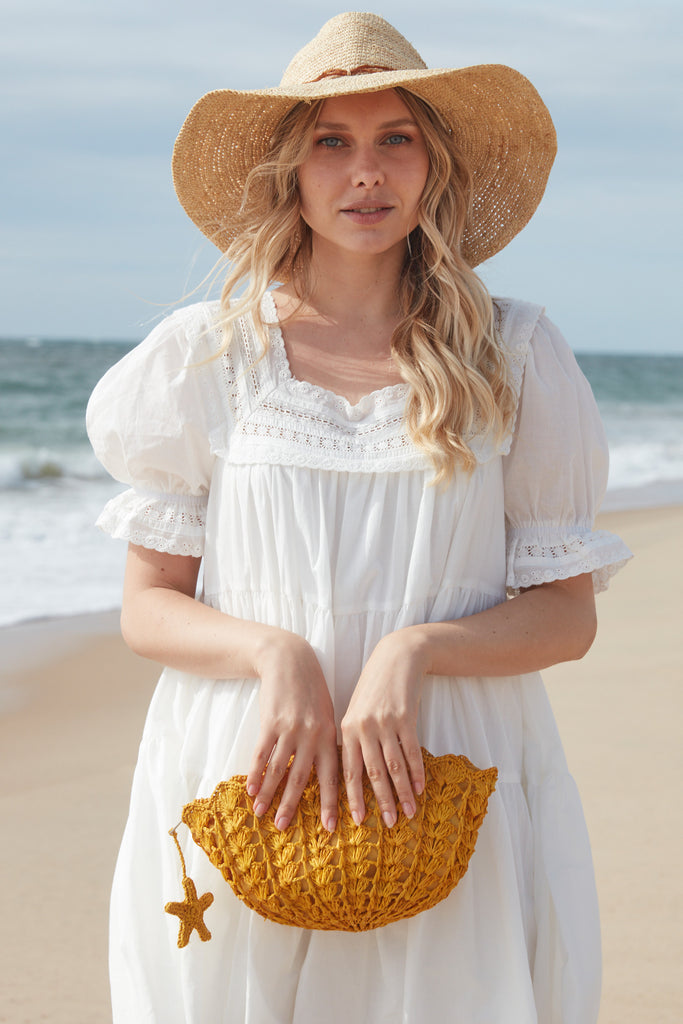 Model on a beach holding our Shelley clutch in Sunflower