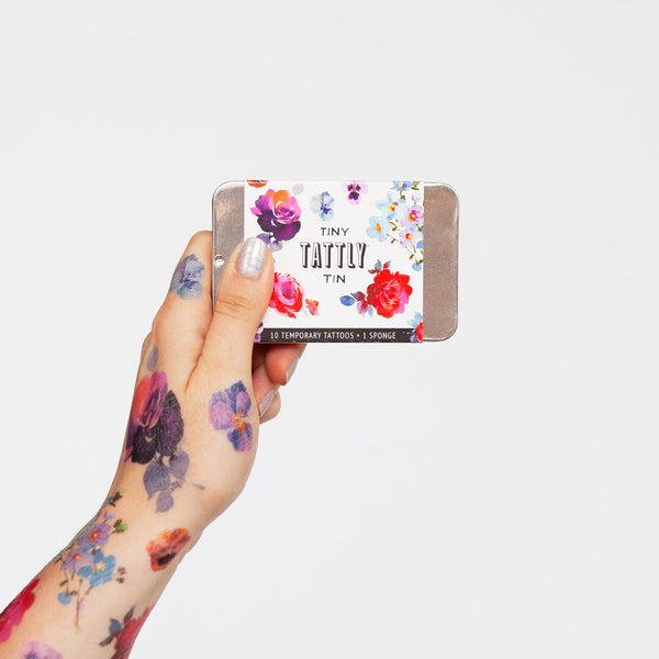Tattooed model hand holding tiny tin of flower tattoos