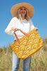 Model holding sunflower colored crocheted open weave carryall with leather handles