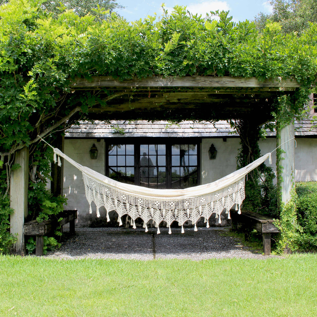 Hand-knotted natural cotton hammock set up between columns in a yard